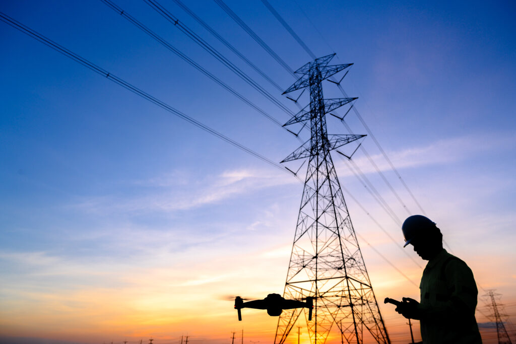 Silhouette of an electrical engineer flying a drone inspecting electrical lines