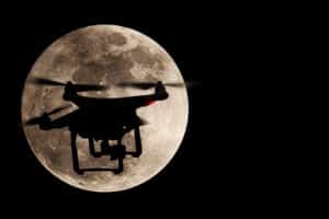 Night time photo of a drone silhouetted against the moon
