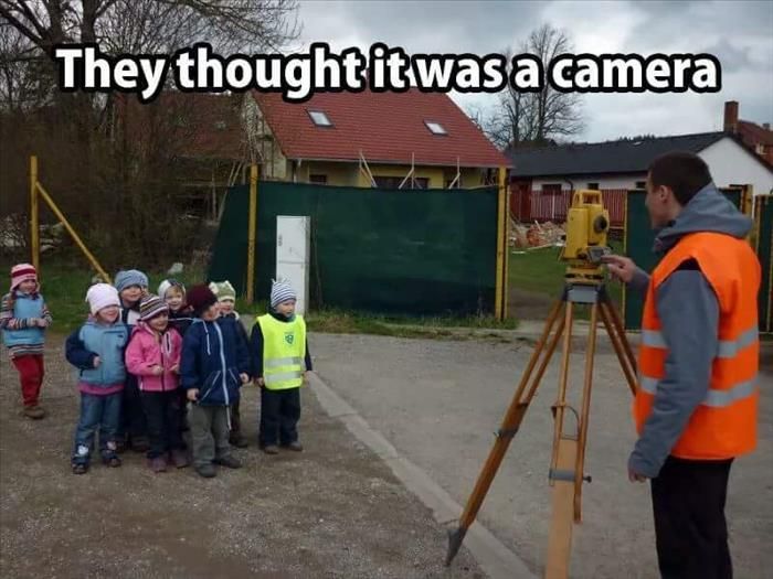 A humorous scene of a surveyor setting up a tripod-mounted instrument while a group of young children stand in a line, posing as if for a photo. The text reads, 'They thought it was a camera.